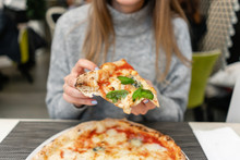 A Woman Is Eating Neapolitan Pizza From Wood-burning Stove. Lunch In An Italian Restaurant. Table Near To A Large Window. Margarita And Four Cheese