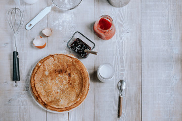 Breakfast with russian bliny or thin sweet crepes, jam and yogurt on a rustic wooden table in daylight