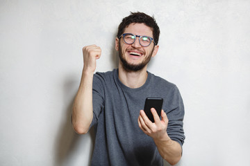 Portrait of young happy man using smartphone, over white textured background.