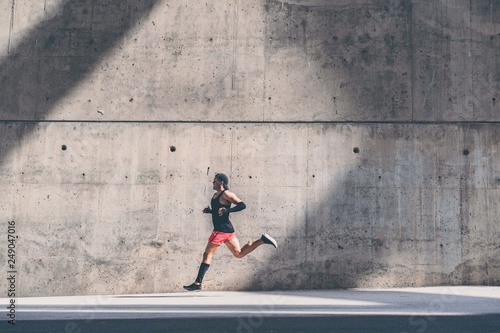 Fotografía Muscular Male athlete sprinter running fast,exercising outdoors,jogging outside against gray concret background with copy space area for text message or ad content