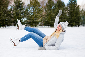 young woman falling down while ice skating at winter rink