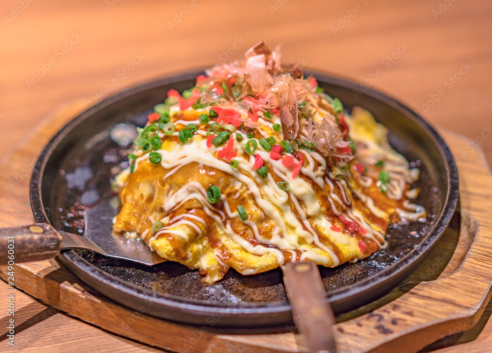 Japanese okonomiyaki covered with katsuobushi leek mayonnaise and bulldog sauce served on a hot plate with spatulas.