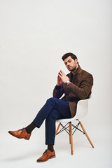 Irresistible man. Stylish dark-haired man sitting on a chair and looking at camera isolated over white background