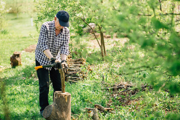 Senior man in baseball cap with axe chopping wood. Elderly arborist man working in garden. Active retirement lifestyle concept.