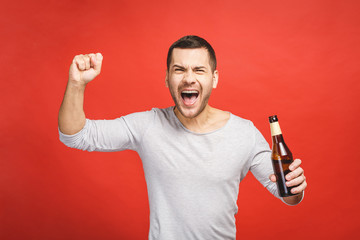 A young guy with a beard isolated on a red background holds a bottle of beer. Watching football match.