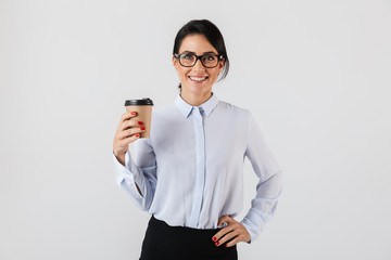 Wall Mural - Image of young secretary woman wearing eyeglasses drinking coffee from paper cup in the office, standing isolated over white background