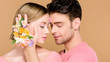 © LIGHTFIELD STUDIOS - handsome boyfriend touching face of  girlfriend with flowers on face isolated on beige