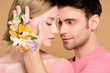 © LIGHTFIELD STUDIOS - handsome man touching face of beautiful girlfriend with flowers on face isolated on beige