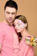 © LIGHTFIELD STUDIOS - handsome man embracing girlfriend with flowers on face isolated on beige