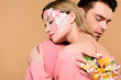 © LIGHTFIELD STUDIOS - boyfriend with alstroemeria flowers on hand embracing attractive girlfriend with flowers on face isolated on beige