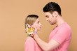 © LIGHTFIELD STUDIOS - side view of tender man with alstroemeria flowers on hand touching face of attractive girlfriend isolated on beige