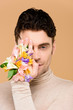 © LIGHTFIELD STUDIOS - man with alstroemeria flowers on hand covering one eye isolated on beige