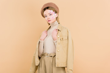 woman with flowers on face wearing beret and standing isolated on beige