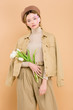 © LIGHTFIELD STUDIOS - trendy woman in beret holding bouquet of flowers isolated on beige