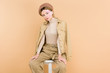 © LIGHTFIELD STUDIOS - trendy woman in beret sitting on chair isolated on beige