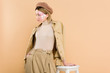 © LIGHTFIELD STUDIOS - stylish woman in beret standing near chair isolated on beige