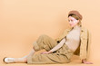 © LIGHTFIELD STUDIOS - stylish girl in beret posing while sitting on floor isolated on beige