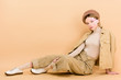 © LIGHTFIELD STUDIOS - trendy girl in beret posing while sitting on floor isolated on beige