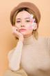 © LIGHTFIELD STUDIOS - serious woman with flowers on face looking at camera isolated on beige