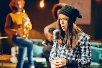 Canvas Print - Band practice in home studio. Woman singing while rest of the band playing instruments.