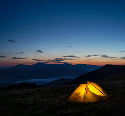Wall Mural - orange lighted tent in mountains under evening sky