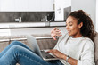 © Drobot Dean - Photo of brunette african american woman using laptop, while lying on sofa in bright living room