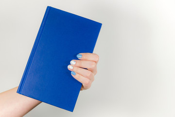 Closeup view of one beautiful female hand holding blue paper book with empty cover. Horizontal color photography.