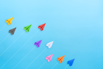 multicolored paper planes on blue background, business competition concept with copy space