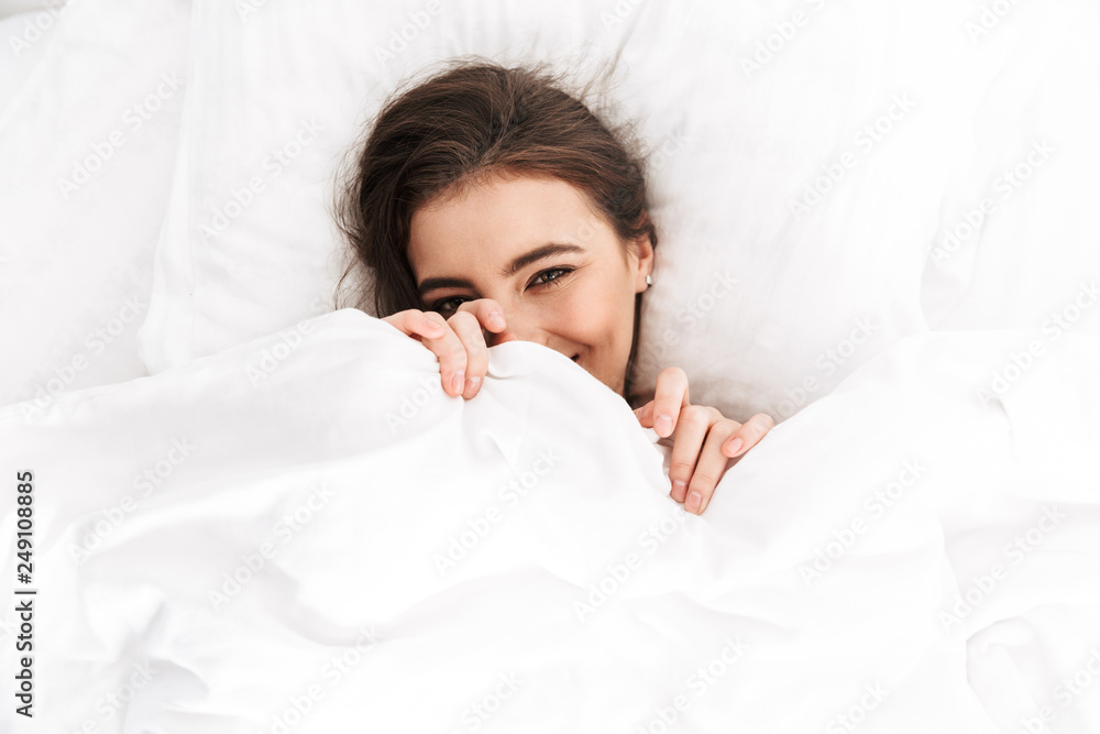 Photo from above of cute woman 20s smiling, while lying in bed on white pillow after sleep or nap - obrazy, fototapety, plakaty 