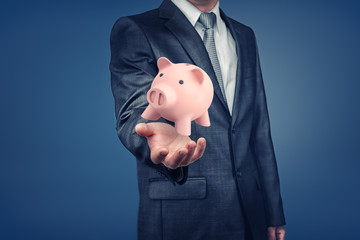 A businessman with hidden face shows a hand with a pink piggy bank hovering above it.