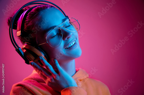 Photographie Fashion pretty woman with headphones listening to music over red neon background at studio