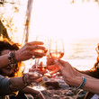 © simona - people drinking at party. group of friends white wine in hand toasting with glasses. close up on hands and drinks - beautiful scenic sunset and ocean in background for outdoor leisure activity