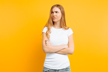 Portrait of an upset young girl standing with folded arms and offended face, on yellow background