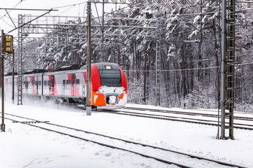 Red electric train moves through winter forest