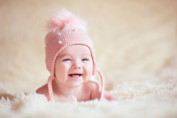 happy baby girl wearing stylish knitted hat lying in bed close up. childhood.