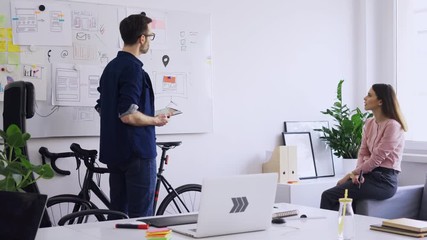 Two web developers discussing ideas and drawing on whiteboard in small office