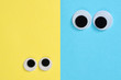 Two pair googly eyes on blue-yellow background look at each other. Mad funny toys eyes close up.
