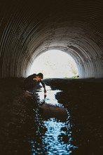 Side View Of Boy Looking Into Water While Crouching In Tunnel