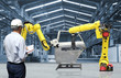 © sittinan - Man hand holding tablet with automate wireless Robot arm in smart factory background. Mixed media of welding robot in the automotive parts industry