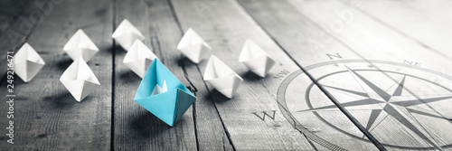 Fotomural Blue Paper Boat Leading A Fleet Of Small White Boats With Compass Icon On Wooden