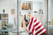 © Seventyfour - Side view portrait of proud American woman holding flag while watching sports match at workplace in office, copy space
