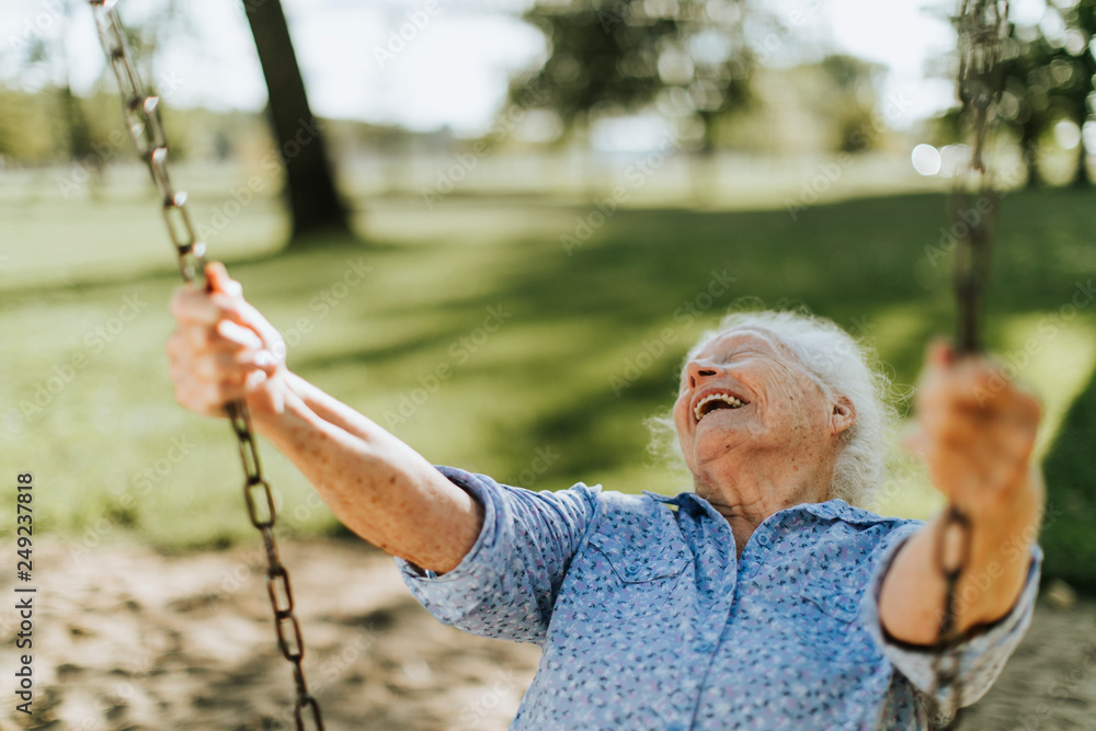 Cheerful senior woman on a swing at a playground - obrazy, fototapety, plakaty 