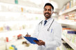 © Syda Productions - medicine, pharmacy and healthcare concept - smiling indian male doctor or pharmacist in white coat with stethoscope and clipboard over drugstore background