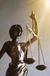 lady justice or justitia blindfolded figurine holding balance scales - law and legal symbol - with sun rays light leak