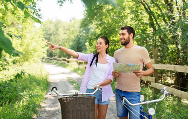 Poster - travel, trip, leisure and lifestyle concept - happy young couple with map and bicycles looking for location at country in summer