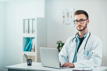 Wall Mural - Portrait of Young Doctor on the Job working on laptop