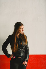 Wall Mural - Girl dressed in black leather posing inside a garage with white and red background wall.