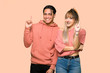 © luismolinero - Young couple showing and lifting a finger in sign of the best over pink background