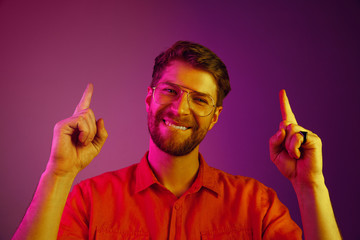 Happy business man standing and pointing up on pink studio background. Beautiful male portrait. Young emotional man. Human emotions, facial expression concept. Neon, retro, synth wave and art style