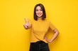© luismolinero - Young woman over yellow wall smiling and showing victory sign